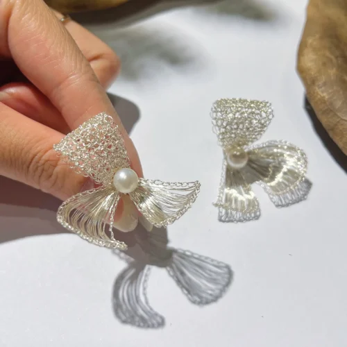 Close-up of handmade silver-tone wire bow earrings with pearl-look center beads