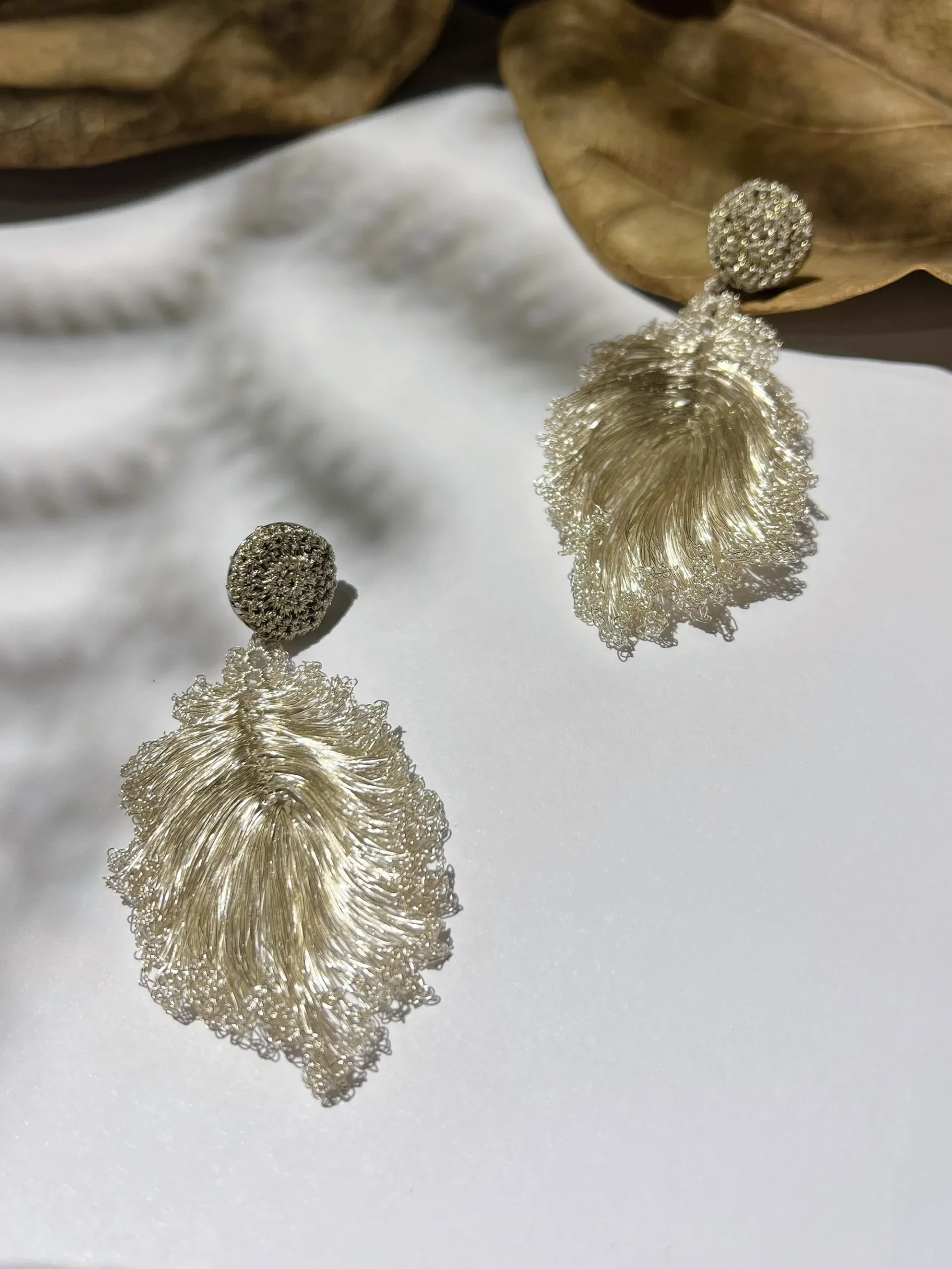 Pair of handwoven silver-tone leaf drop earrings displayed on white