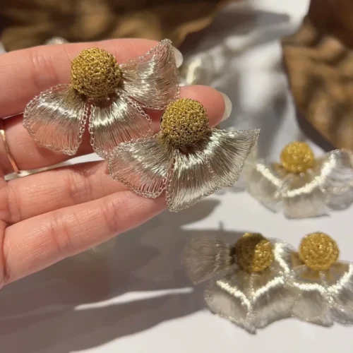 Close-up of handmade silver-tone wire flower earrings with gold-tone centers