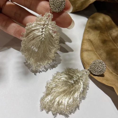 Close-up of handmade silver-tone wire leaf earrings held in a hand