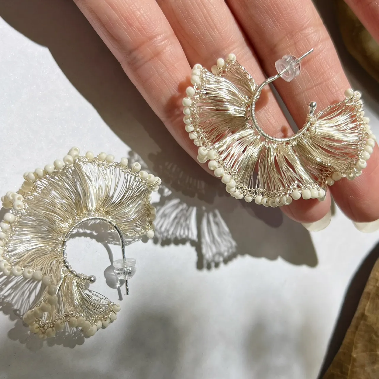 Close-up of ivory beaded silver-tone wire ginkgo hoop earrings
