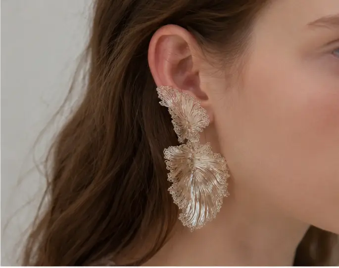Close-up of OREYNE botanical fan palm statement earrings worn