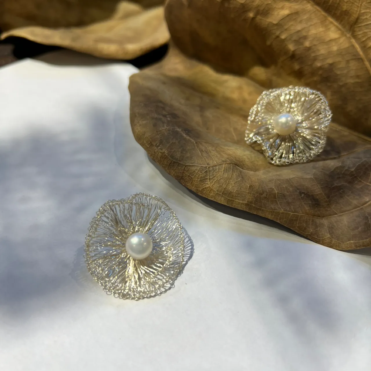 Pair of silver-tone wire flower stud earrings displayed beside dried leaves