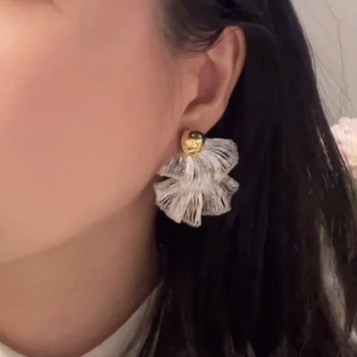 Woman wearing a silver-tone layered fan statement earring with a gold-tone ball stud