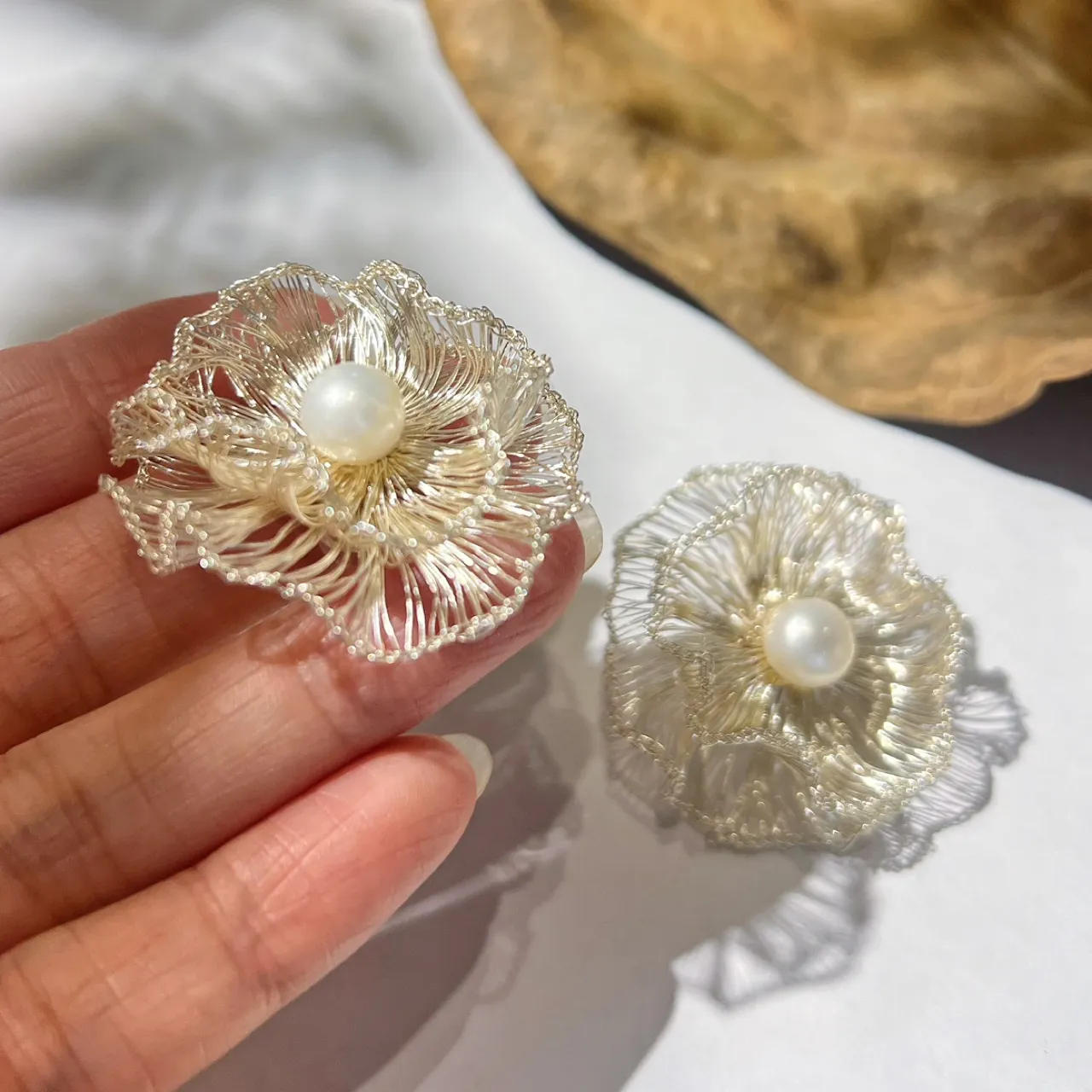 Close-up of handmade silver-tone wire flower earrings held in a hand