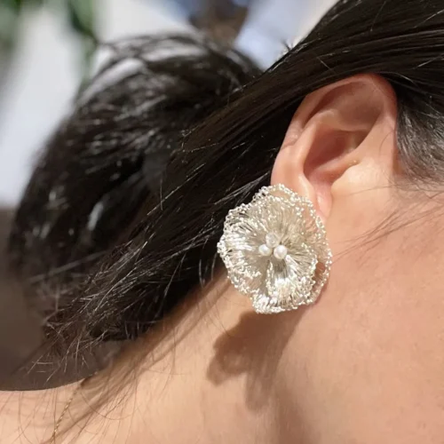 Woman wearing a handmade silver-tone wire flower statement earring with pearl-look accents