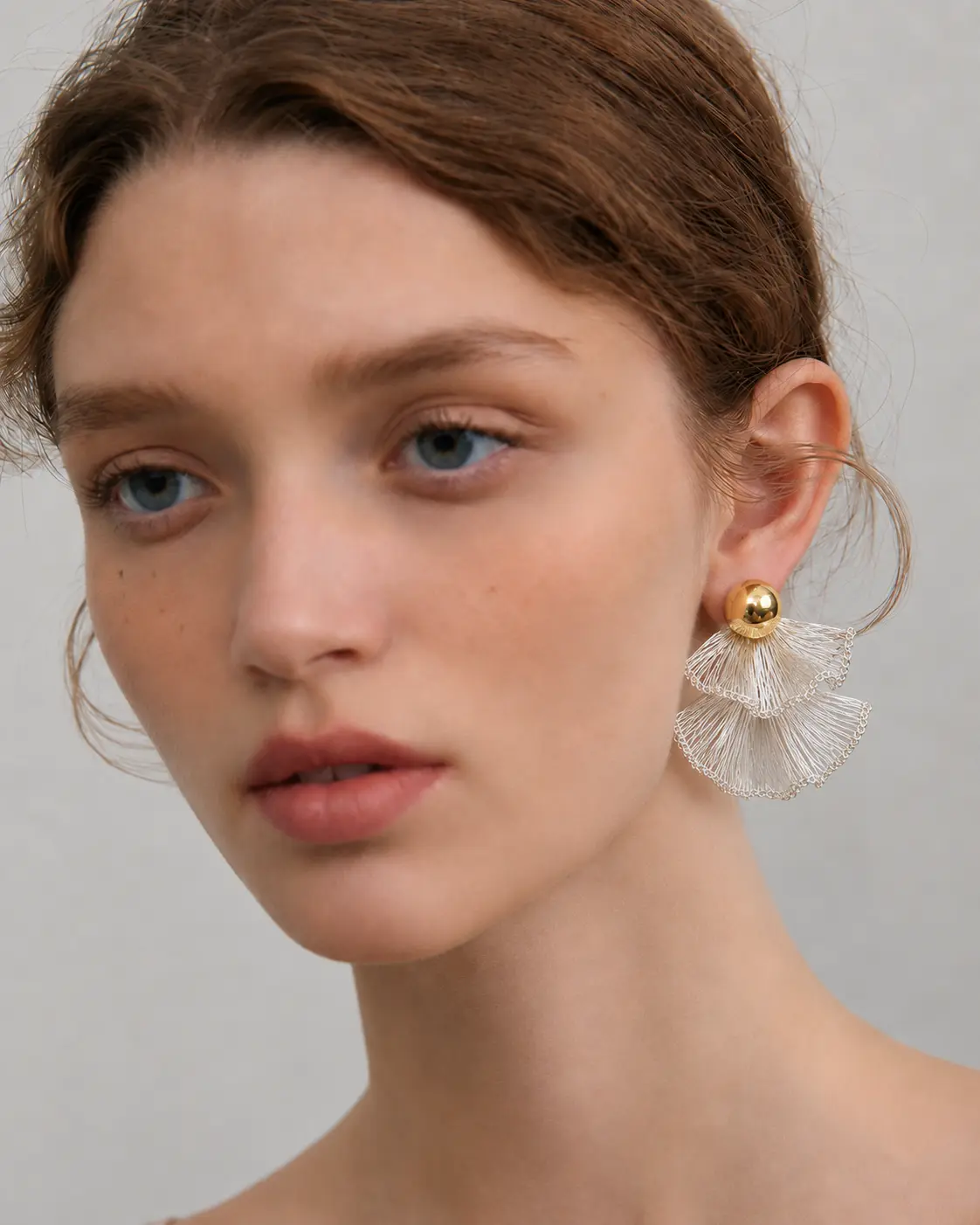 Woman wearing a silver-tone layered fan statement earring with a gold-tone ball stud
