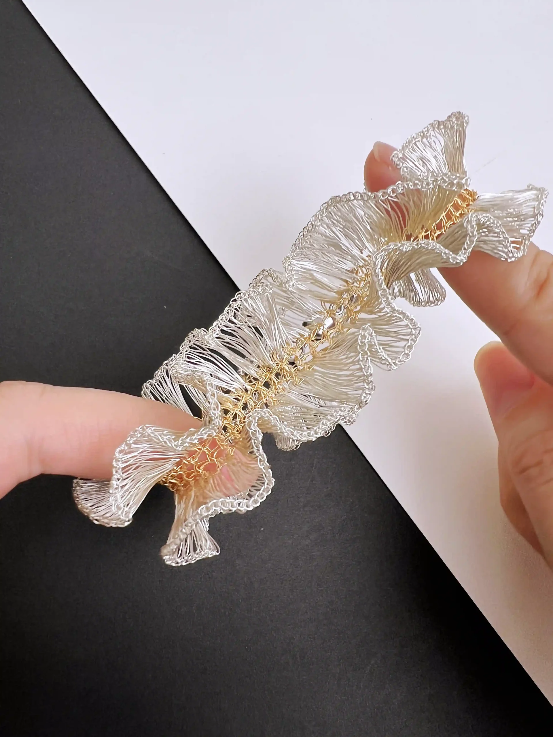 Hands holding a silver-tone and gold-tone handwoven wire bracelet, showing its ruffled edge and woven texture