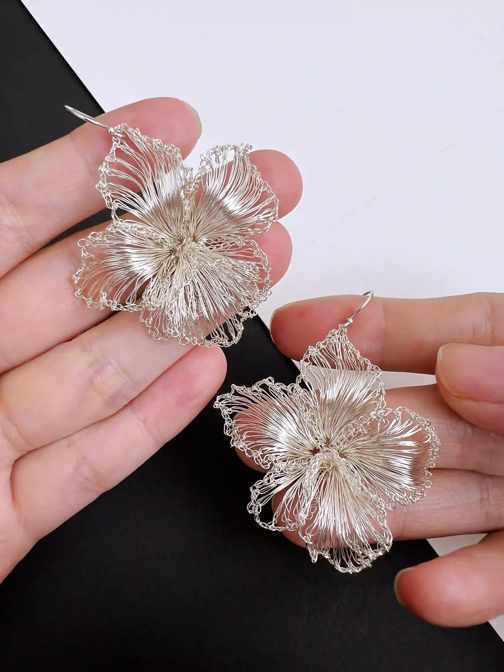 Handheld pair of silver-tone handwoven wire blossom earrings with open sculptural petals