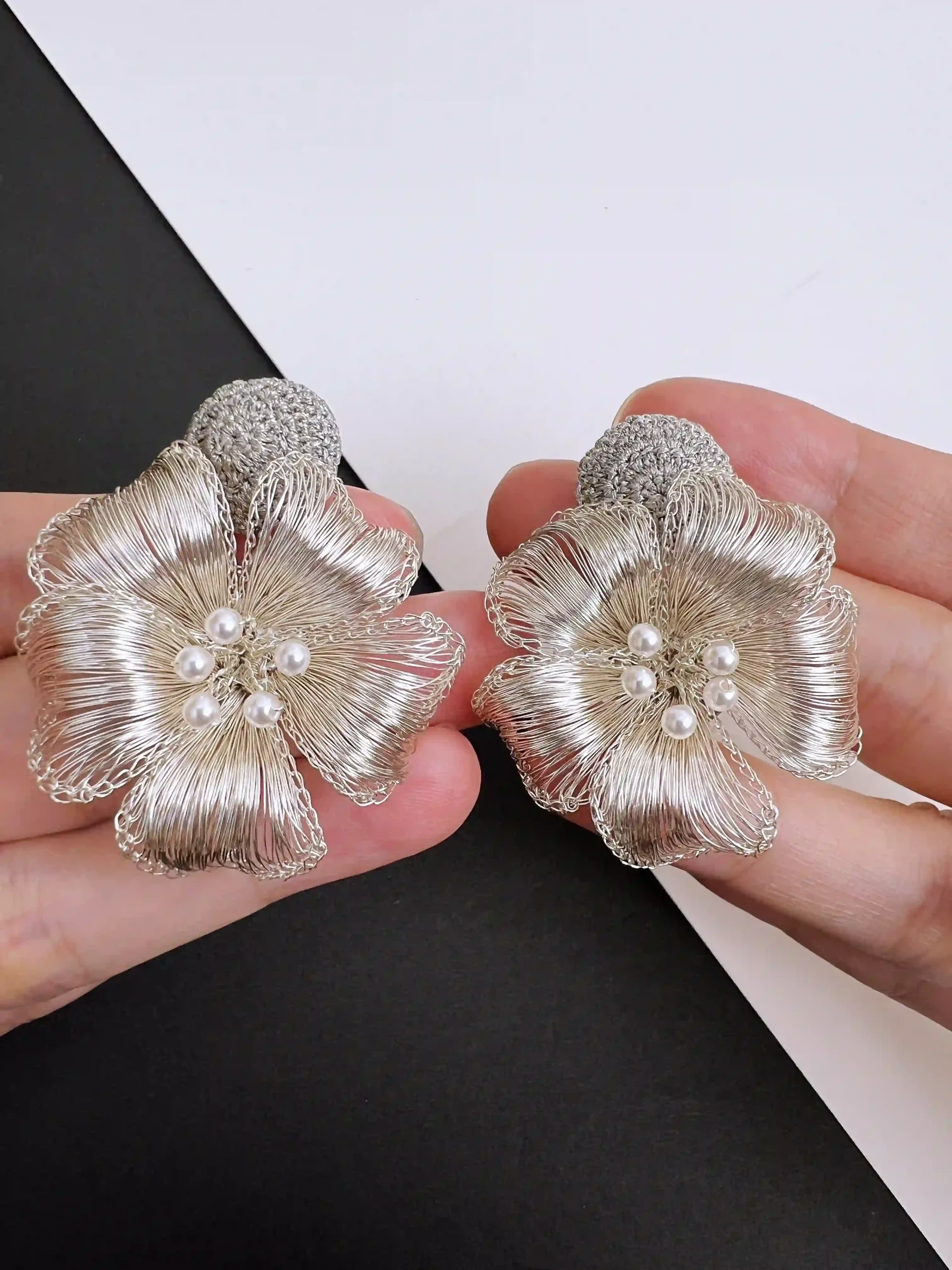 Close-up of a silver-tone handwoven wire flower earring with layered petals and clustered pearl-look center accents