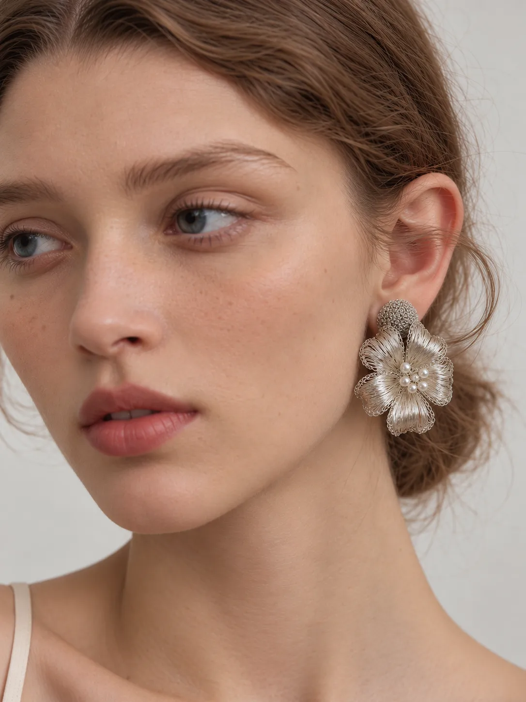 Front worn view of an openwork flower drop earring with a round woven stud and pearl-look floral center