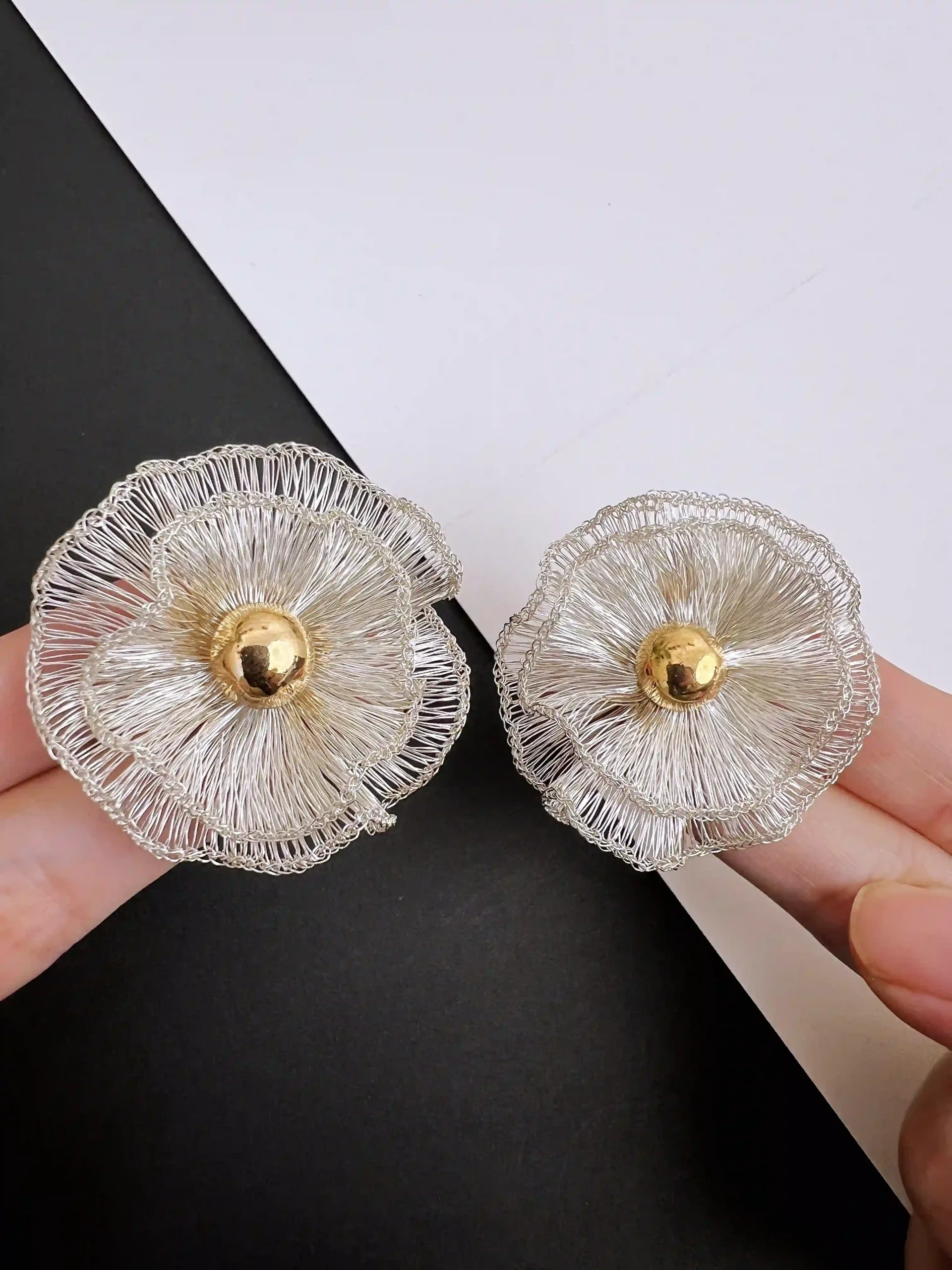 Handheld close-up of red handwoven wire flower earrings with layered petals and gold-tone centers