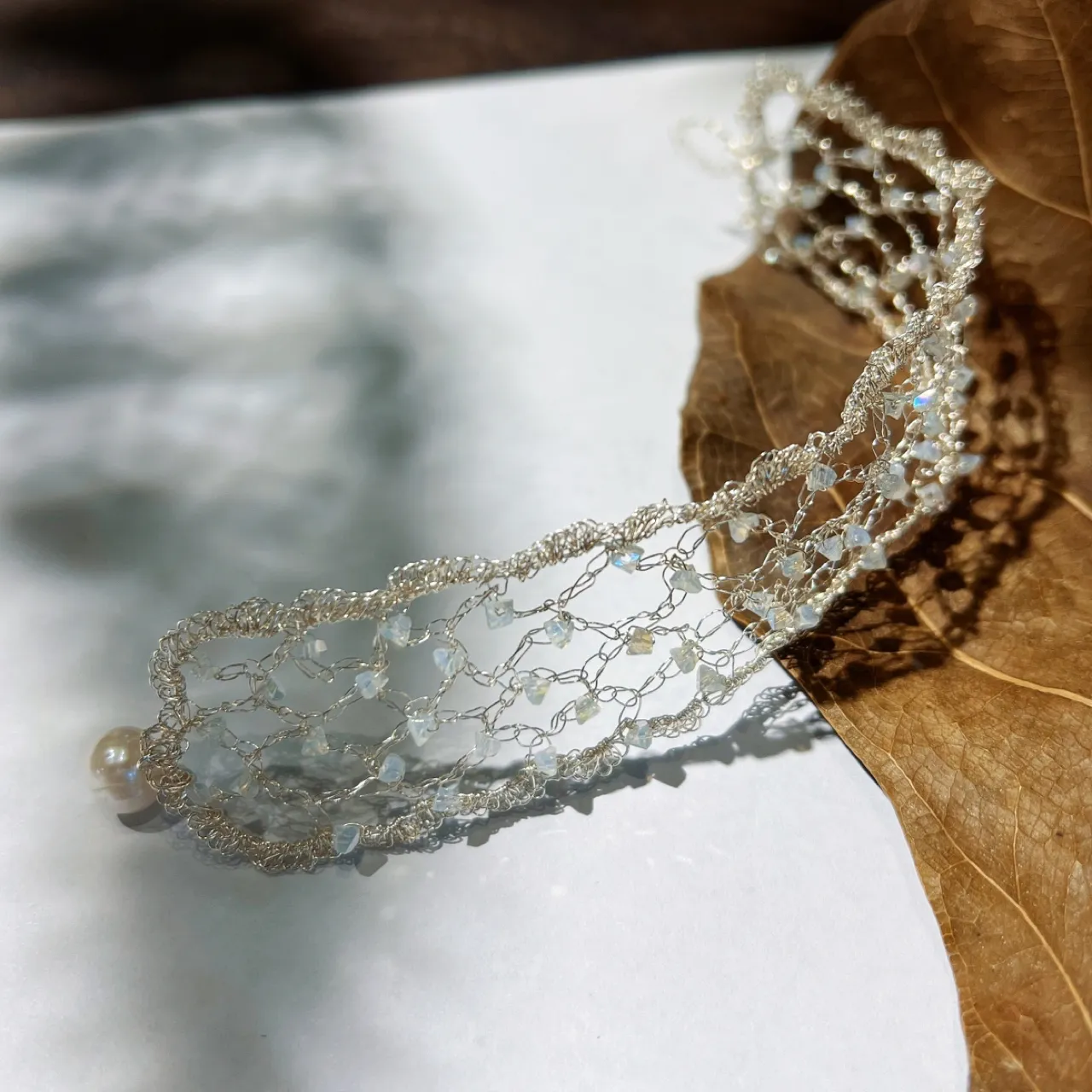 Angled close-up of silver-tone handwoven wire lace jewelry with translucent decorative accents