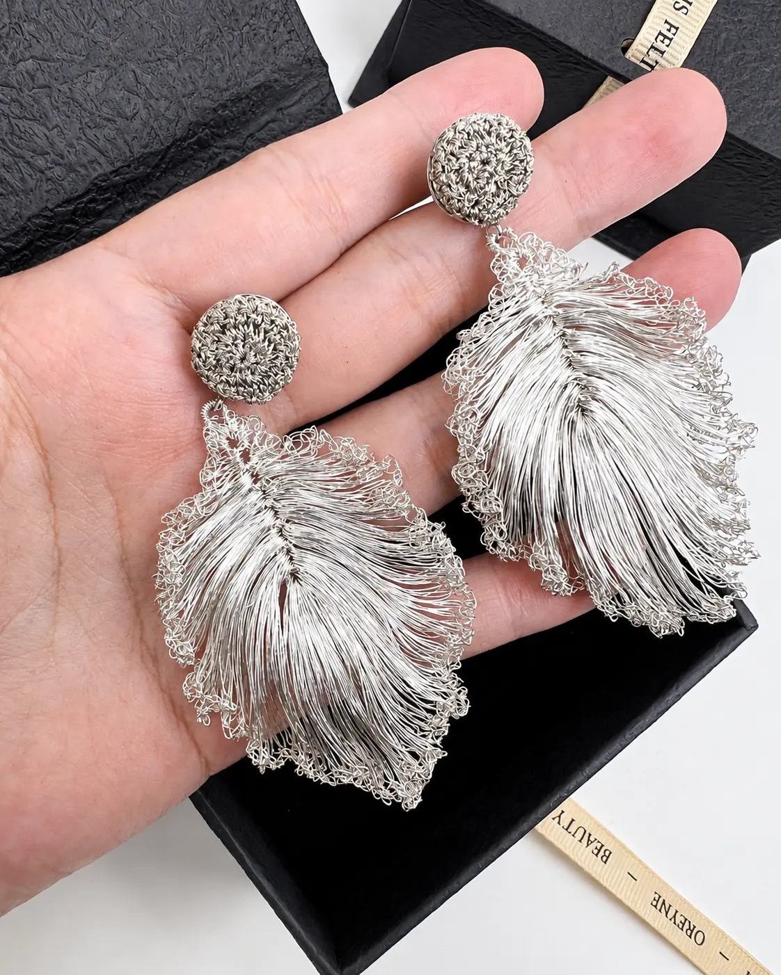 Close-up of handmade openwork leaf earrings held in a hand