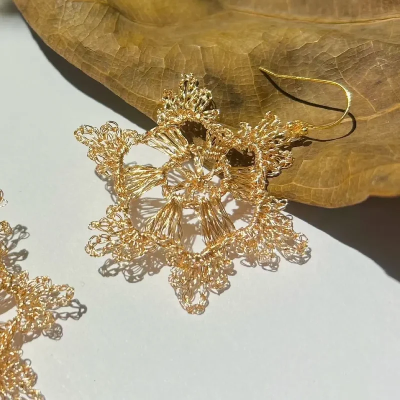 Close-up of a gold-tone handwoven wire earring with layered radial sections and detailed looped metallic edges.