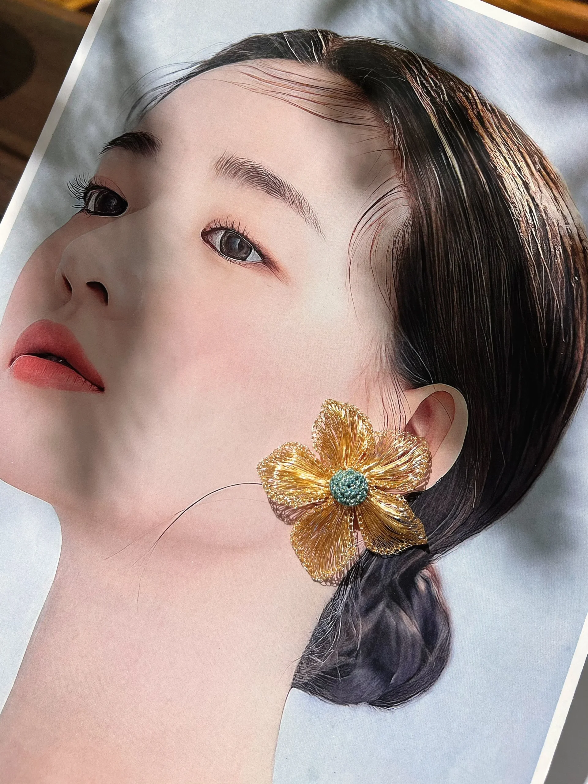 Gold-tone wire flower statement earring styled over an editorial portrait to demonstrate its visual scale
