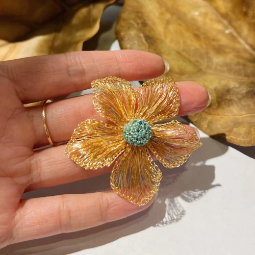 Handheld close-up of a gold-tone wire flower statement earring with open petals and a teal textured center