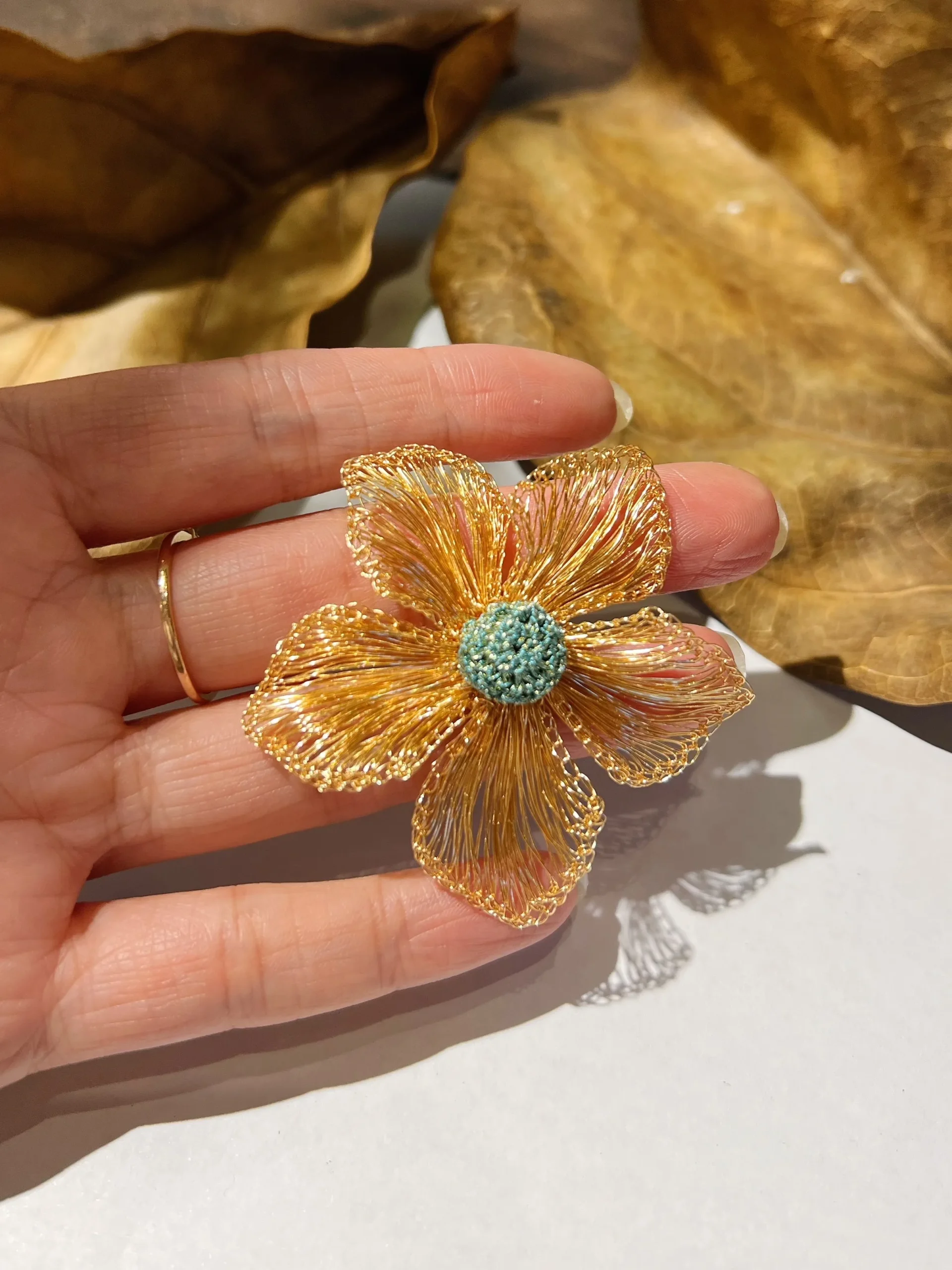 Handheld close-up of a gold-tone wire flower earring with open petals and teal center
