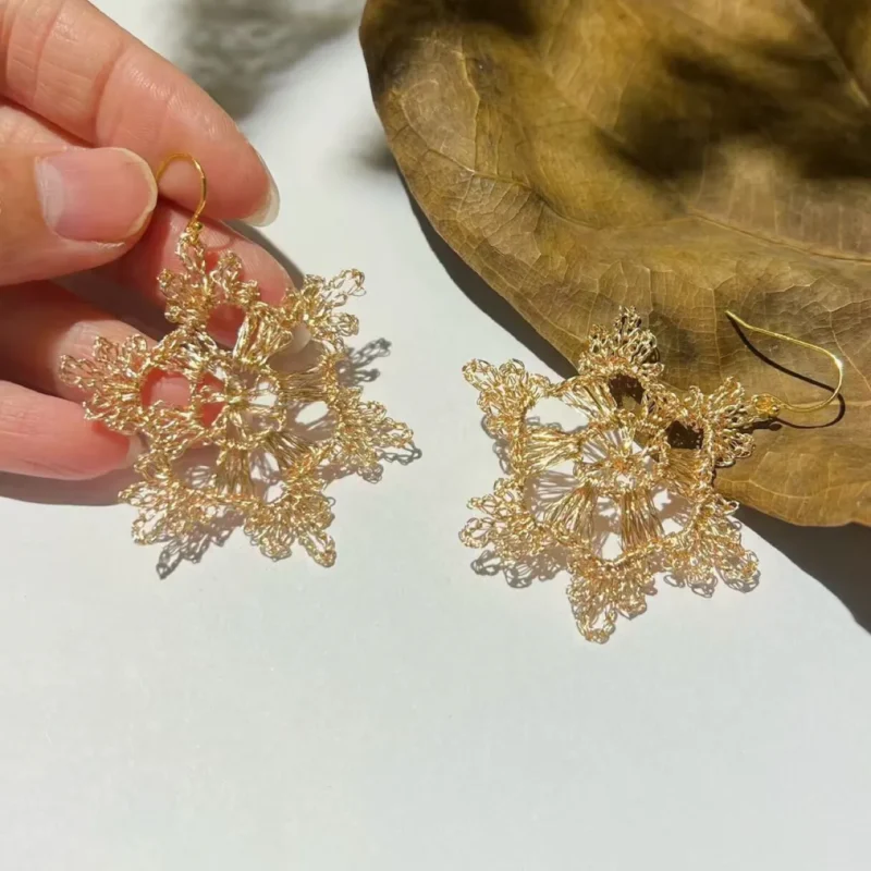 Handheld pair of gold-tone handwoven wire statement earrings with intricate open radial construction.