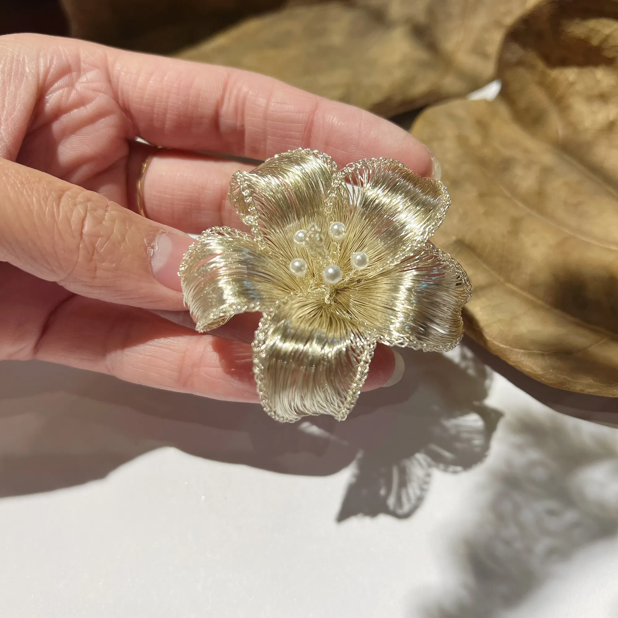 Close-up of handwoven metallic wire petals and pearl-look accents on OREYNE sculptural brooch