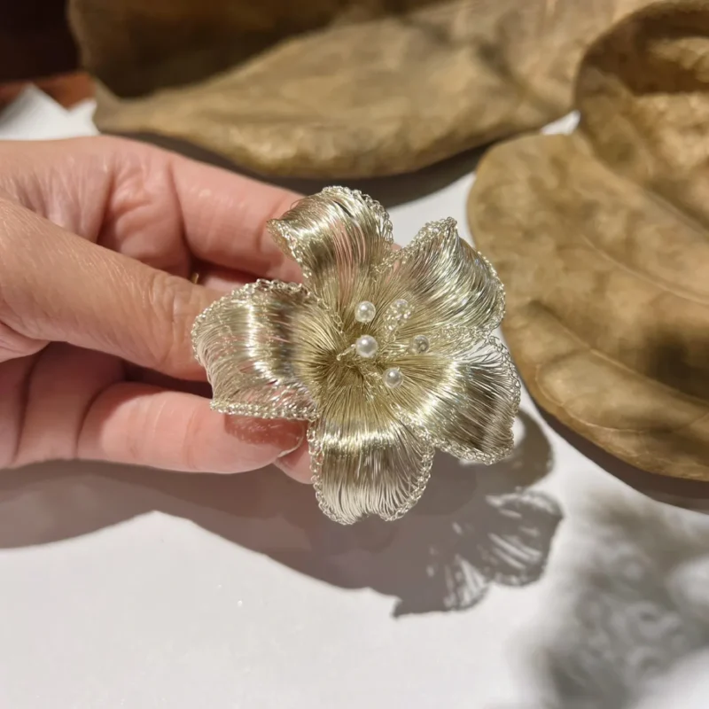 Angled handheld view of a gold-tone sculptural wire brooch with pearl-look details.