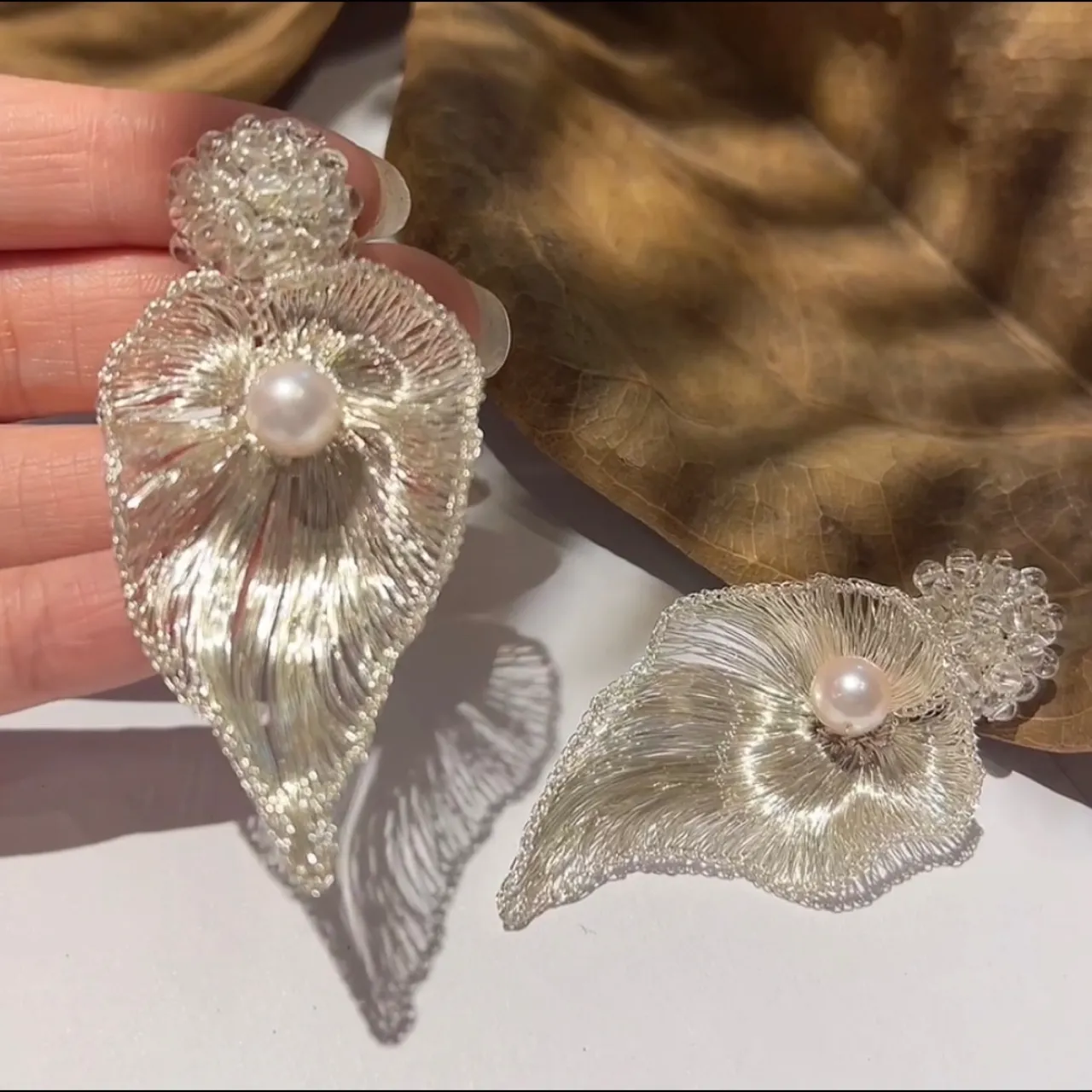Pair of Lunelle Fold silver-tone sculptural handwoven metal earrings held by hand
