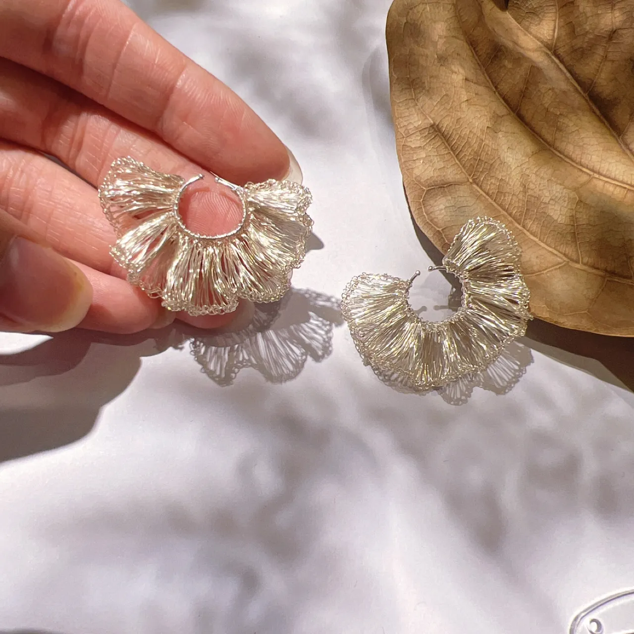Handheld openwork hoop earring showing the layered ruffle structure and woven metallic strands