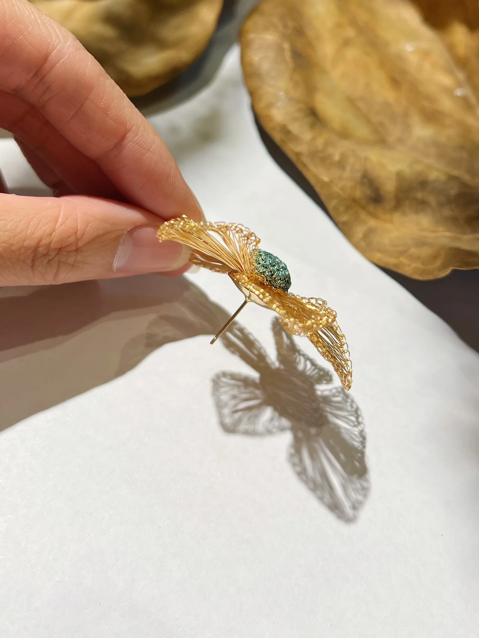 Side view of a handwoven gold-tone wire flower earring with raised teal center and visible post