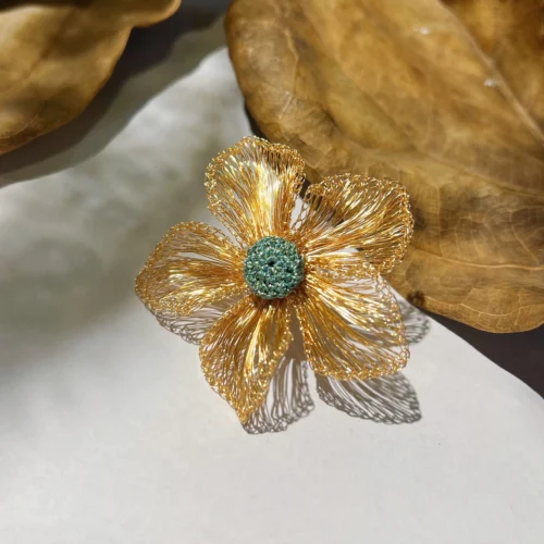 Handwoven gold-tone wire flower statement earring with five open petals and a textured teal center