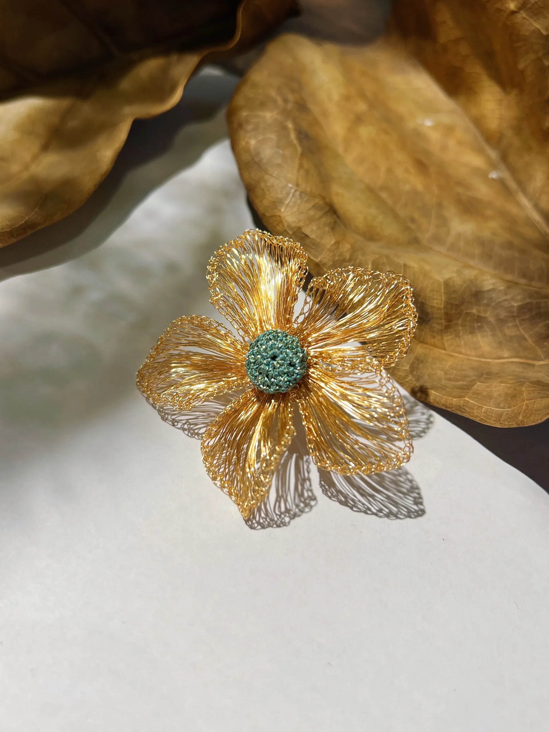 Handwoven gold-tone wire flower statement earring with five open petals and a textured teal center