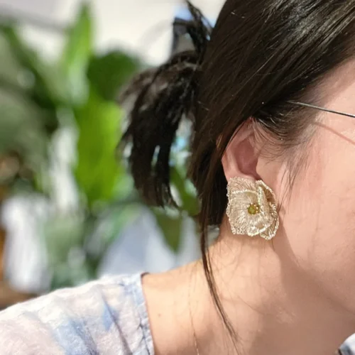 Ivory-tone handwoven wire flower statement earring with a small green bead center worn on the ear