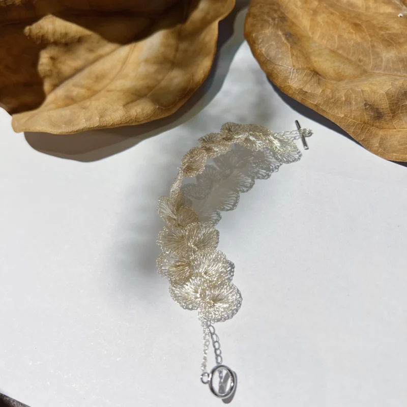 Curved view of a handwoven Fine Silver-Plated Copper Wire flower bracelet showing its linked floral construction and toggle clasp