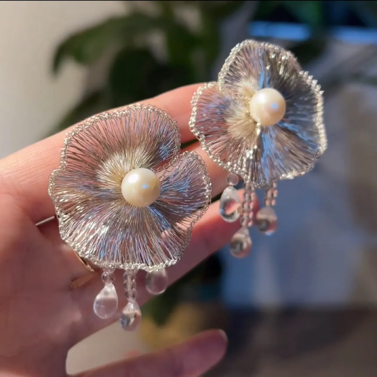 Handheld pair of silver-tone handwoven wire flower earrings with pearl-look centers and clear teardrop dangles