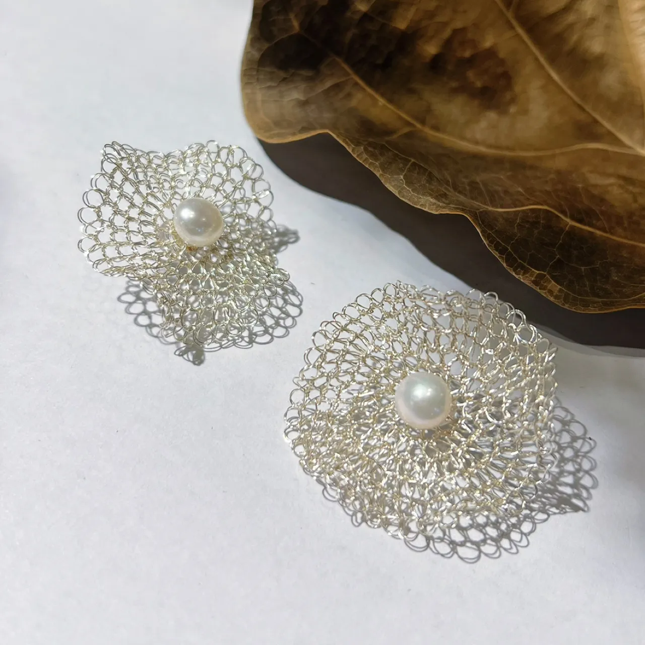 Close-up of handwoven openwork flower earrings with layered petals and pearl-look centers