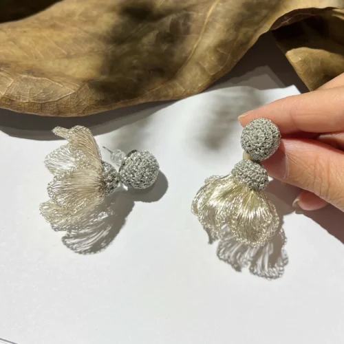 Handheld pair of silver-tone wire petal drop earrings with round woven studs and sculptural floral pendants