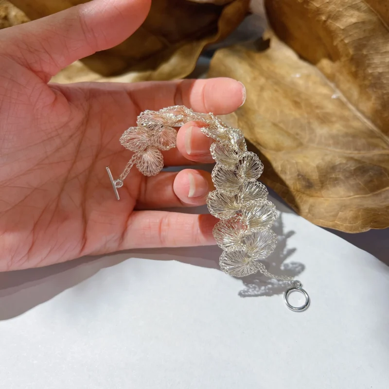 Handheld view of a handwoven Fine Silver-Plated Copper Wire blossom bracelet showing the flexible linked flower construction