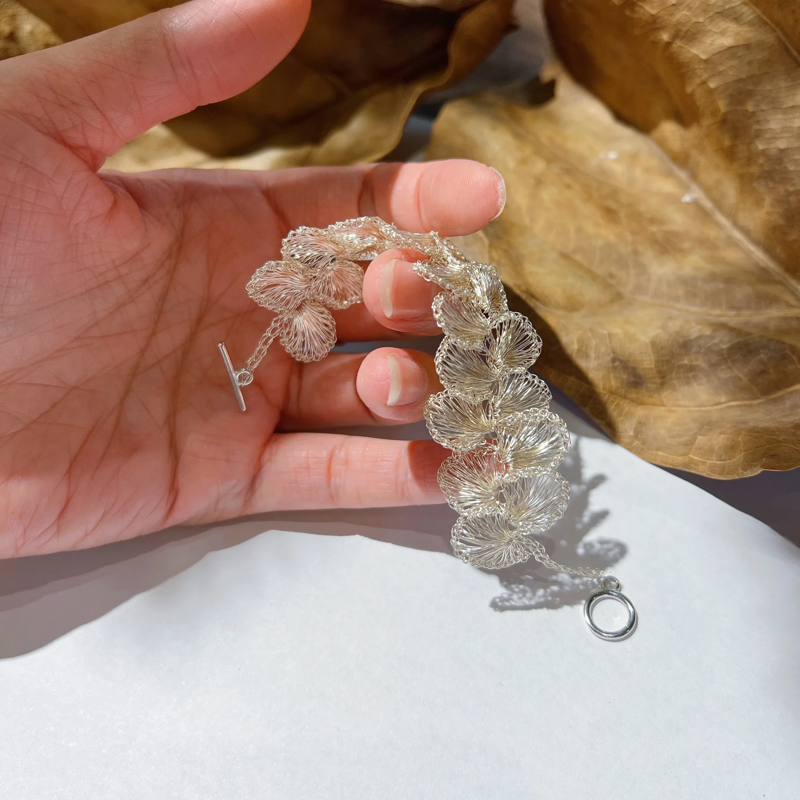 Handheld view of a silver-tone handwoven wire blossom bracelet showing the flexible linked flower construction