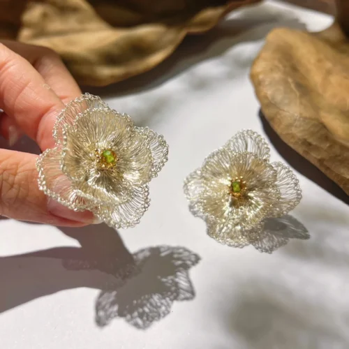 Close-up of handwoven ivory-tone wire flower earrings with layered petals and green bead centers