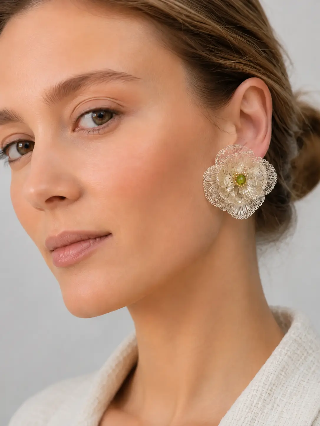 Ivory-tone handwoven wire flower statement earring with a small green bead center worn on the ear