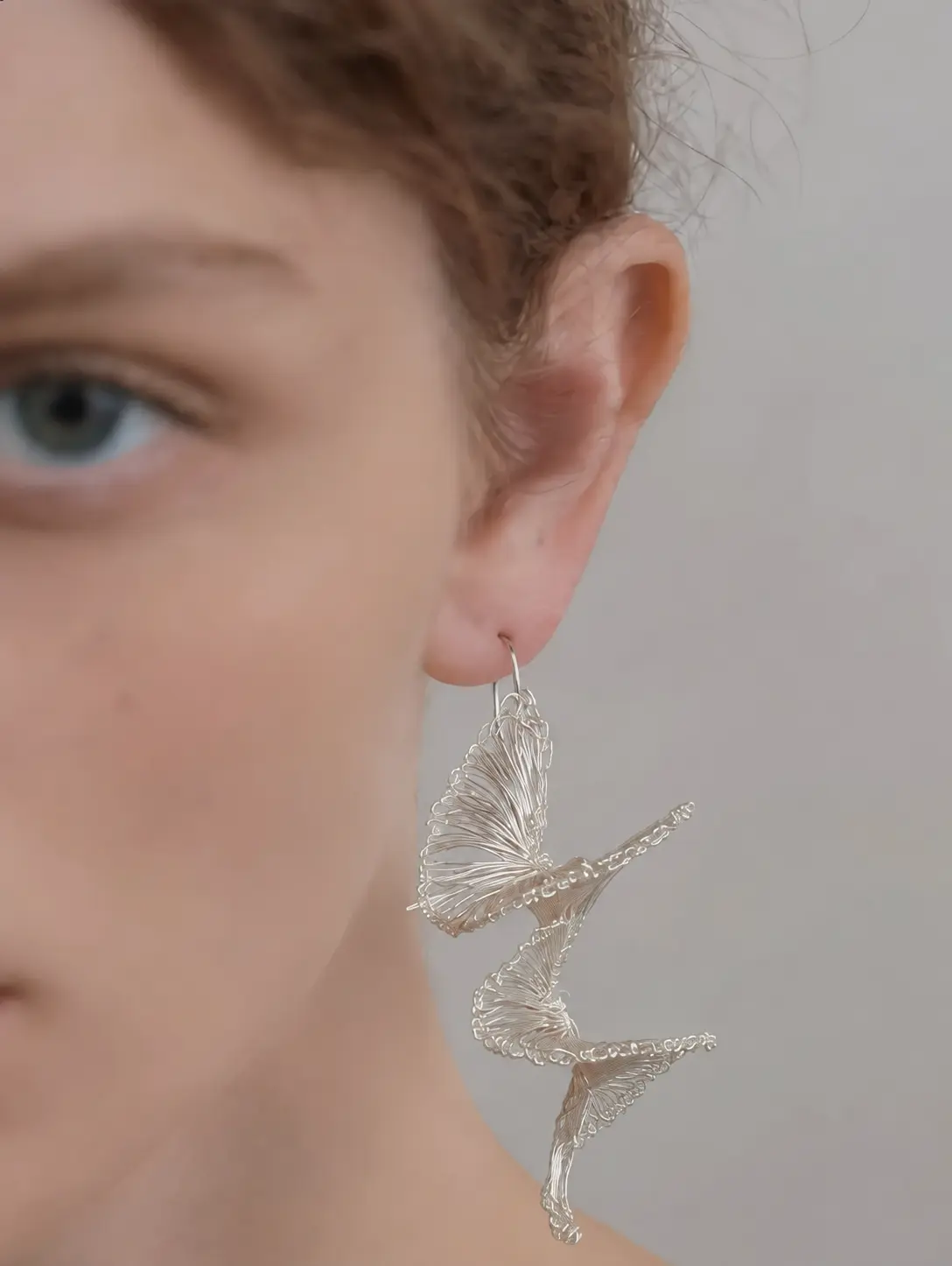 Worn side view of a long openwork earring with cascading sculptural curves