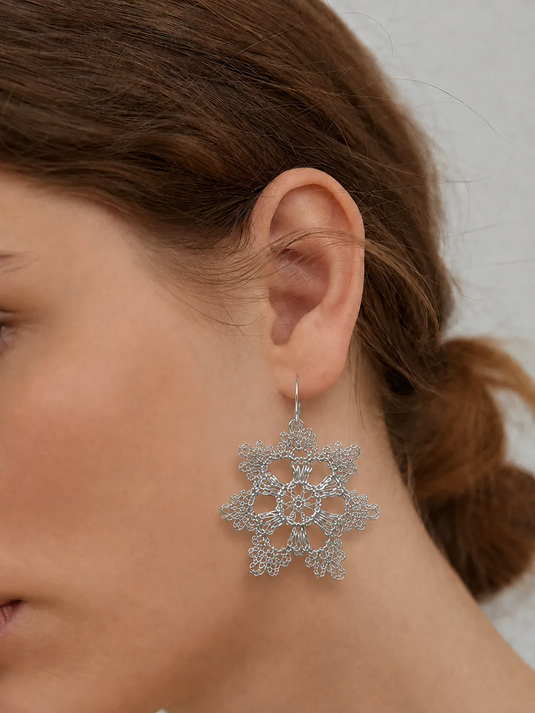 Close-up worn view of a gold-tone sculptural wire earring with intricate radial openwork and looped edge details.