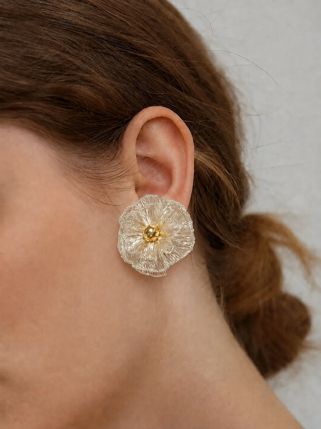 Model wearing a silver-tone handwoven wire flower earring with a gold-tone center