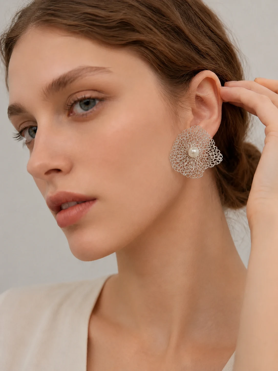 Silver-tone handwoven wire flower statement earring worn close-up with pearl-look center