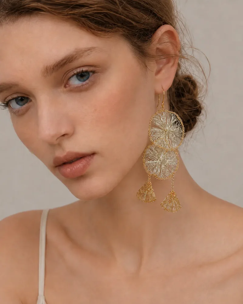 Close-up of OREYNE handwoven gold-tone petal tassel earrings held in hand