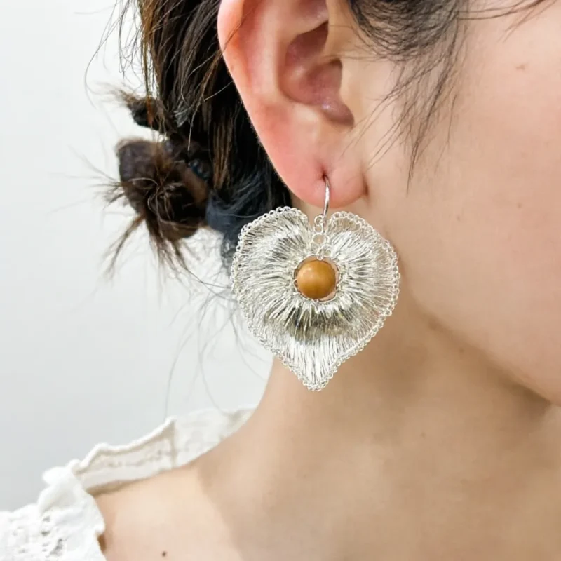 Woman wearing OREYNE handwoven silver-tone heart drop earrings