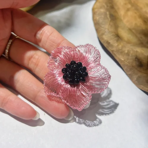 Pink handwoven wire flower statement earring displayed on a hand to show its scale and shape