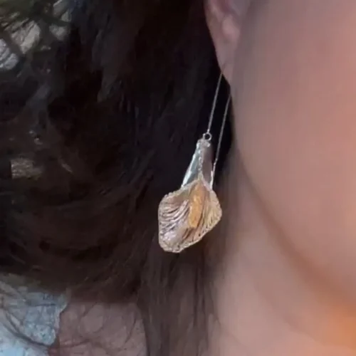 Handwoven silver-tone calla lily threader earring worn against dark hair