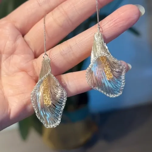 Pair of silver-tone calla lily threader earrings with textured gold-tone centers displayed on a hand