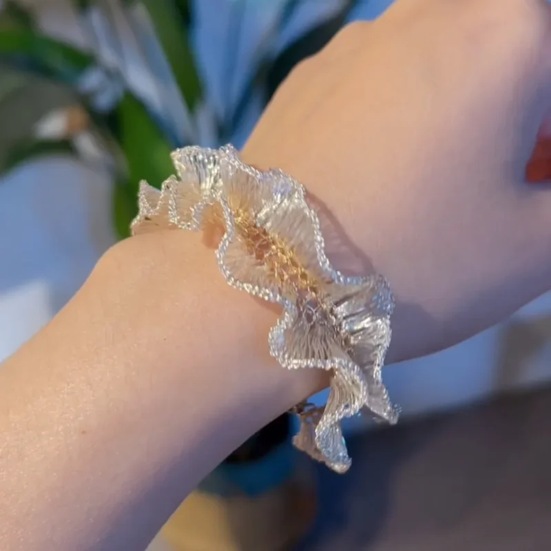 Close worn view of a handwoven Fine Silver-Plated Copper Wire bracelet with sculptural ruffled edges and gold-tone woven details
