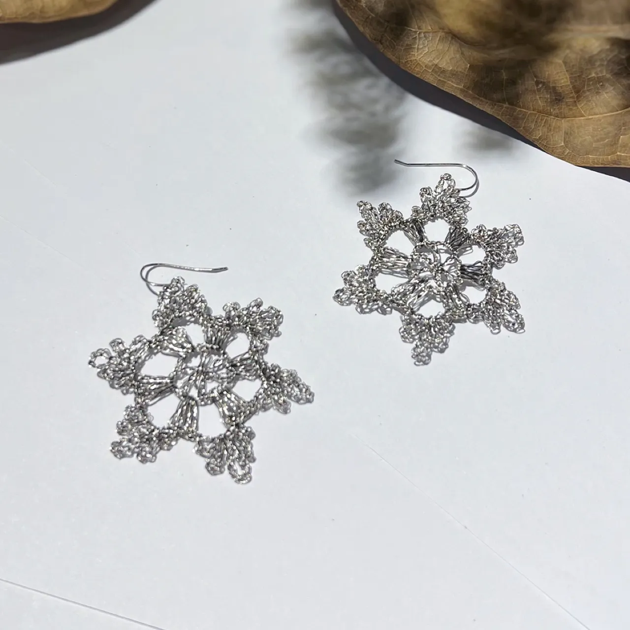 Close-up of a gold-tone handwoven wire earring with layered radial sections and detailed looped metallic edges.